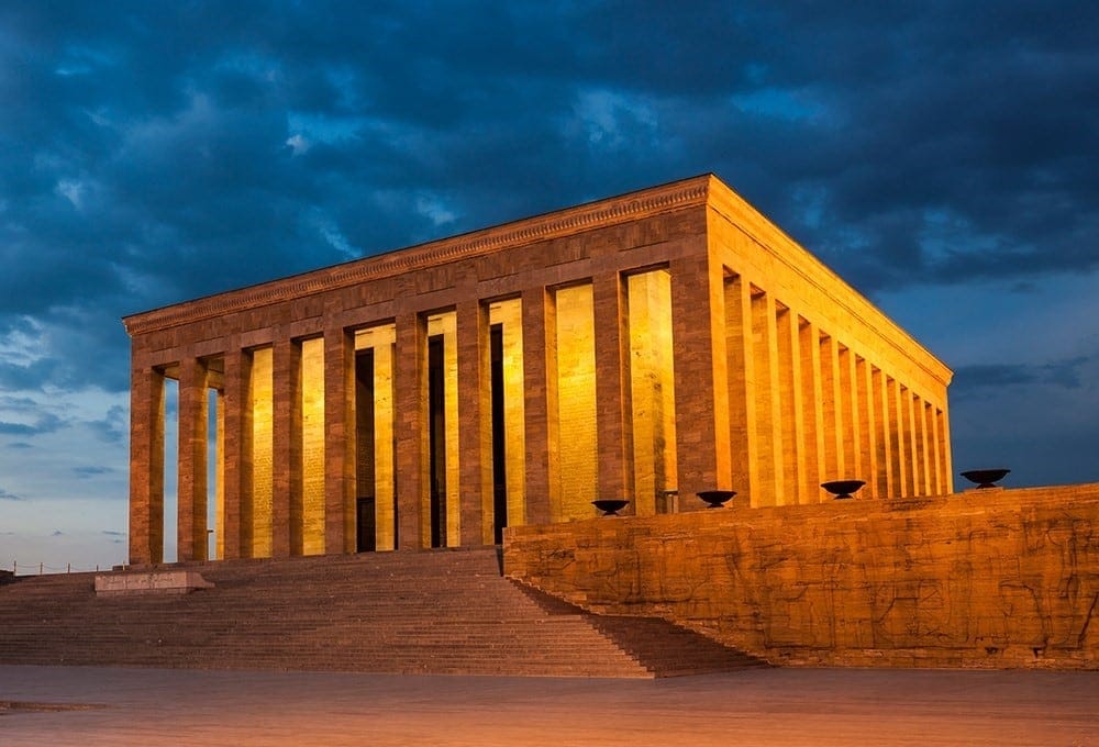 Majestic stone building with illuminated columns against a cloudy sky backdrop.