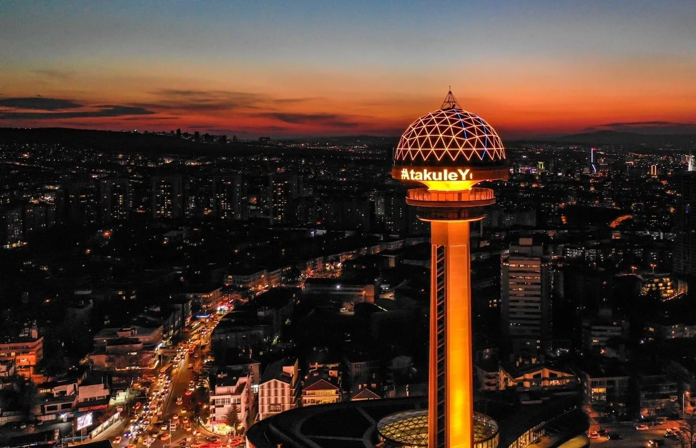 Aerial view of Atakule Tower in Ankara at sunset, with city buildings silhouetted against the colorful sky.