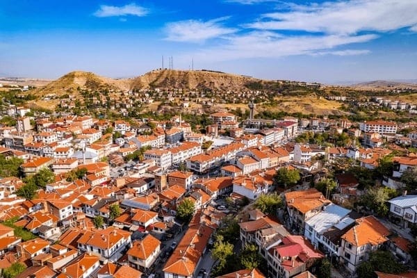 Aerial view of a town with red-roofed buildings surrounded by hills and a clear blue sky.